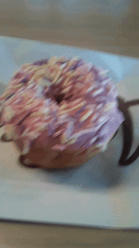 A Donut With Pink Frosting And Sprinkles On Top GIF