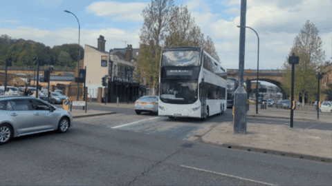 A Double Decker Bus Is Driving Down The Road GIF