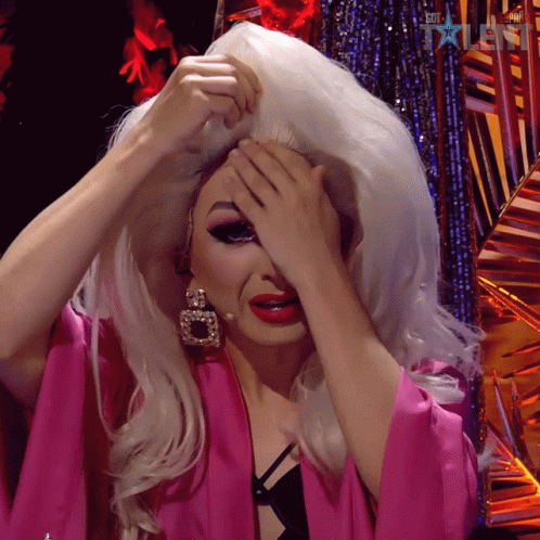 A Drag Queen Covering Her Face With Her Hands While Wearing A Pink Kimono GIF