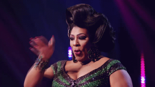 A Drag Queen In A Green And Black Dress Is Making A Funny Face GIF
