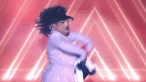 A Drag Queen In A White Dress Is Dancing On A Stage In Front Of A Red Background . GIF