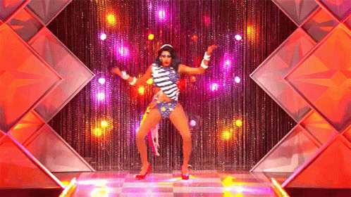A Drag Queen Is Dancing On A Stage In Front Of A Curtain GIF