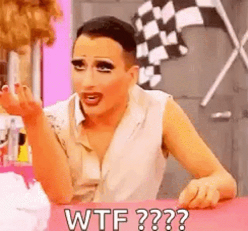 a drag queen is sitting at a table making a funny face and saying `` wtf '' .