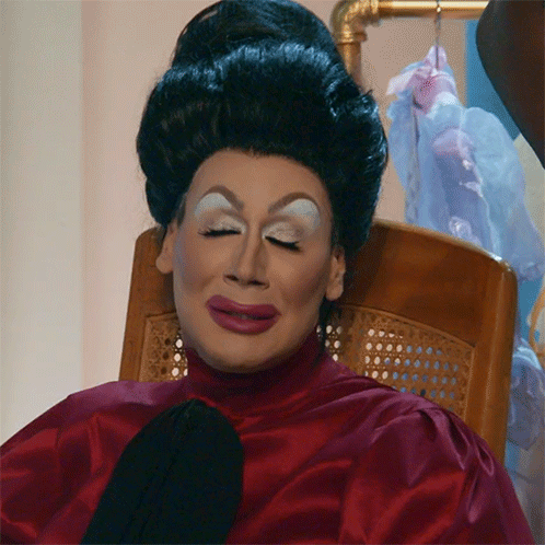 Drag Queen Sitting In Red Top And Black Tie GIF