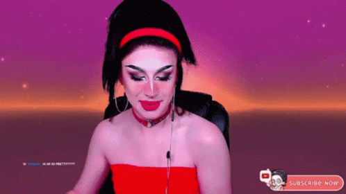 A Drag Queen Is Sitting In Front Of A Purple Background And Holding A Cotton Candy Bar . GIF