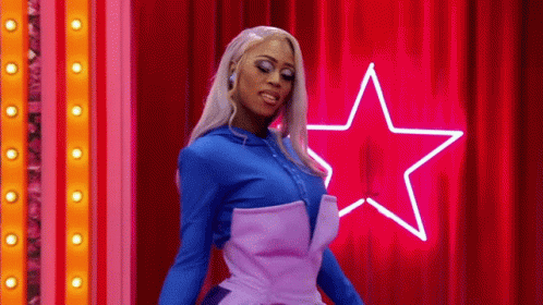 Drag Queen In Front Of Red Curtain And Neon Star GIF