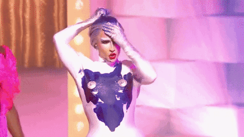 A Drag Queen Is Standing On A Stage With Her Hands On Her Head And A Purple Background . GIF