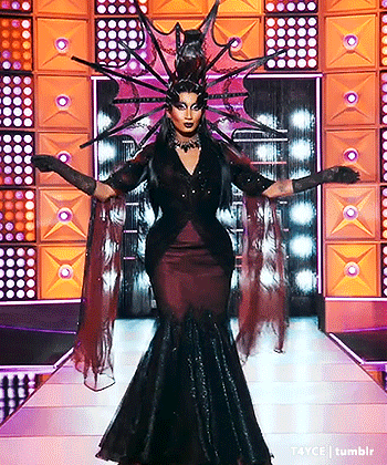 A Drag Queen Is Walking Down A Runway Wearing A Costume That Looks Like A Witch . GIF