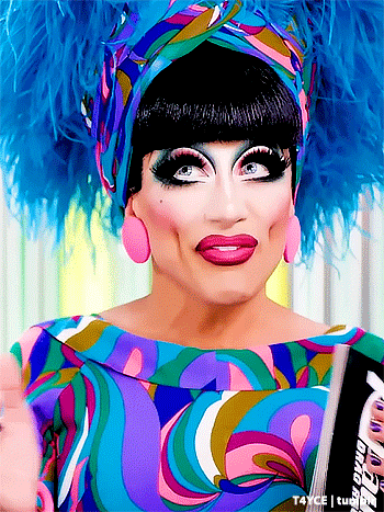 a drag queen is wearing a colorful dress and feathered headpiece