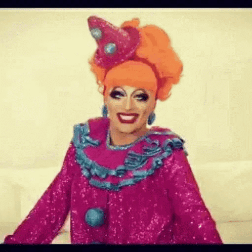 a drag queen is wearing a pink and blue clown costume .