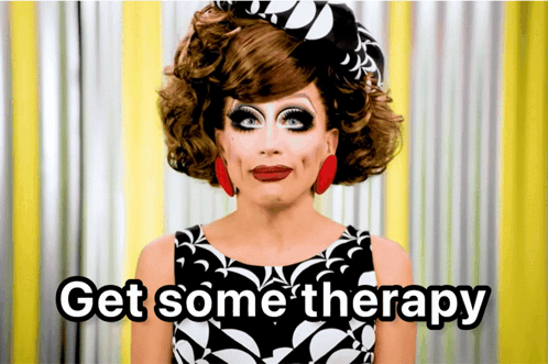 A Drag Queen Says " Get Some Therapy " In Front Of A Yellow Curtain GIF