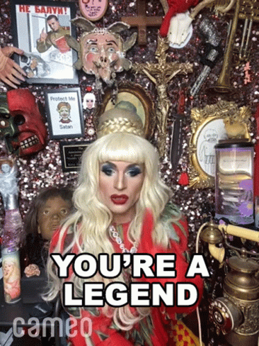 A Drag Queen Says " You 'Re A Legend " In Front Of A Wall Of Memorabilia GIF