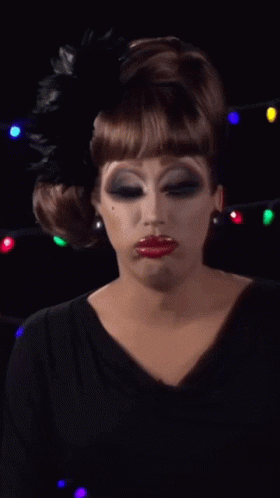 a drag queen wearing a black dress and a black feather in her hair