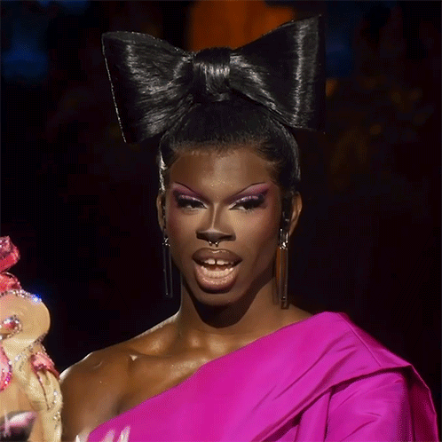 A Drag Queen Wearing A Pink Dress And A Large Black Bow In Her Hair GIF