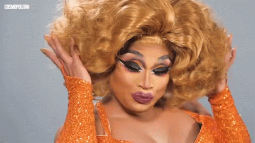 A Drag Queen Wearing An Orange Dress And Gloves GIF
