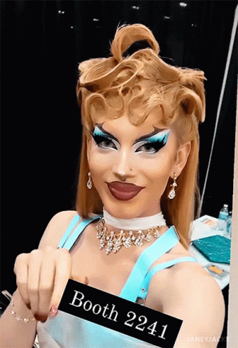 A Drag Queen With A Sign That Says Booth 2241 GIF