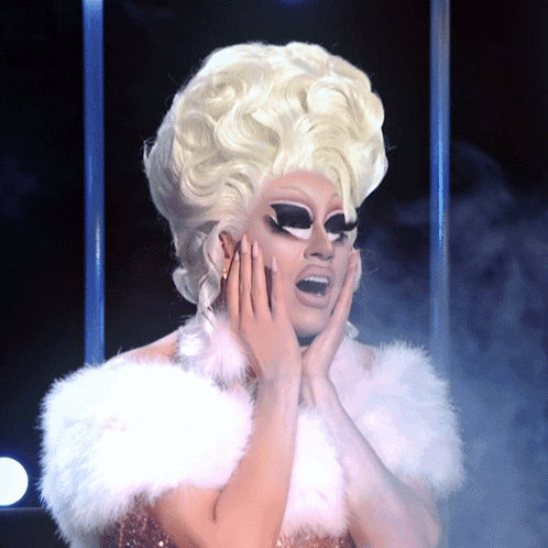 A Drag Queen With Blonde Hair And A White Fur Collar GIF