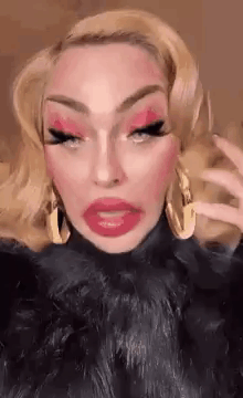 A Drag Queen With Blonde Hair And Red Lips Is Wearing A Black Fur Coat . GIF