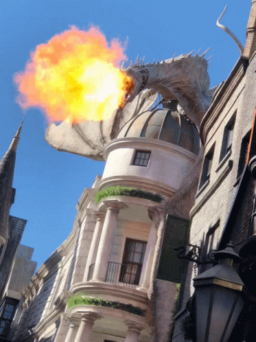 A Dragon With Flames Coming Out Of Its Mouth Is Flying Over A Building GIF
