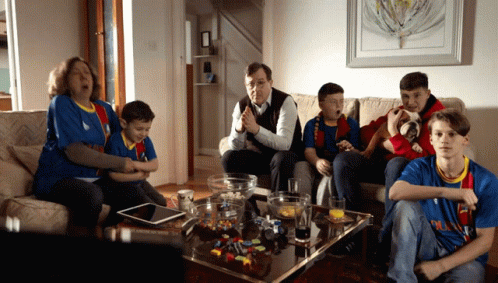 A Family Is Sitting On A Couch Watching A Game And One Of The Boys Is Wearing A Shirt That Says Barcelona GIF