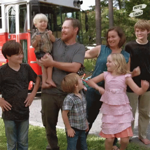 A Family Standing In Front Of A Red Fire Truck With A Sign That Says Wife Swap GIF