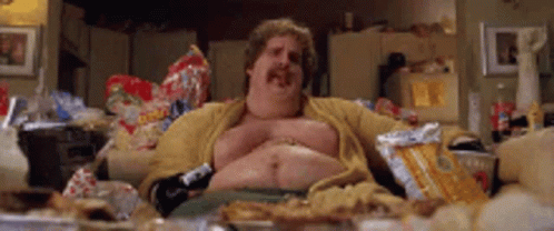 A Fat Man With A Mustache Is Sitting On A Couch Eating Chips . GIF