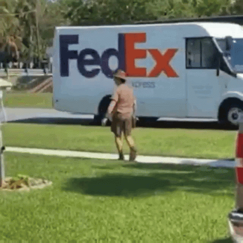 A Fedex Truck Is Parked In The Grass And A Man Is Walking In Front Of It GIF