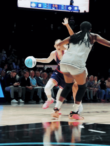A Female Basketball Player Dribbles The Ball While Another Player Tries To Block Her GIF