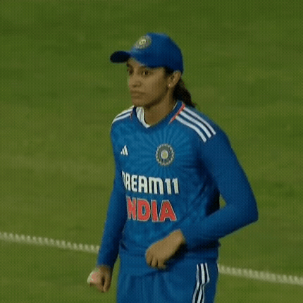 A Female Cricket Player Is Standing On A Field Holding Her Shirt . GIF