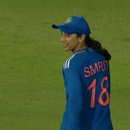 A Female Cricket Player Wearing A Blue Jersey And A Hat Is Walking On A Field . GIF