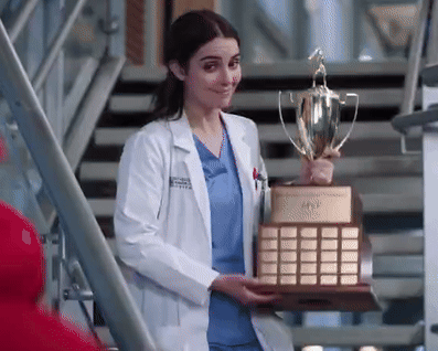 A Female Doctor In A Lab Coat Is Holding A Trophy . GIF