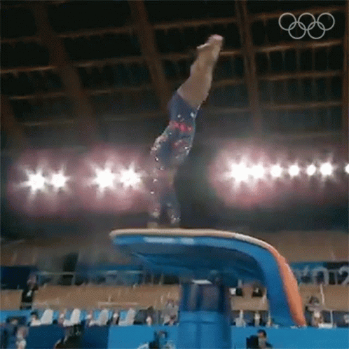 A Female Gymnast Is Doing A Trick On A Balance Beam In Front Of A Crowd . GIF
