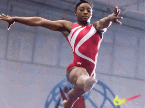 A Female Gymnast Is Doing A Trick On A Balance Beam With A Nike Logo In The Background GIF
