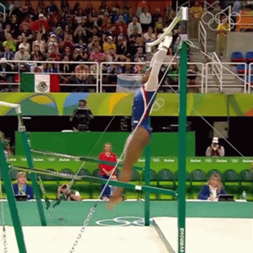 A Female Gymnast Is Doing A Trick On The Uneven Bars While A Crowd Watches . GIF