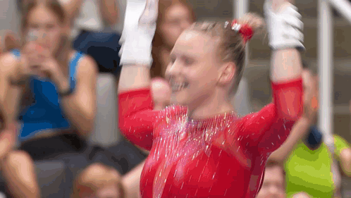 a female gymnast is raising her arms in the air in front of a crowd .