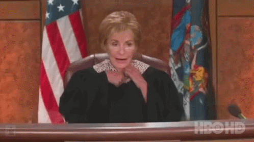 A Female Judge Is Sitting At A Desk In Front Of An American Flag In A Courtroom . GIF