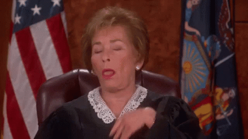 A Female Judge Is Sitting In A Courtroom With Her Eyes Closed And A Flag In The Background . GIF