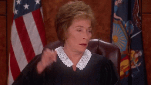 A Female Judge Is Sitting In Front Of An American Flag And Scratching Her Head . GIF