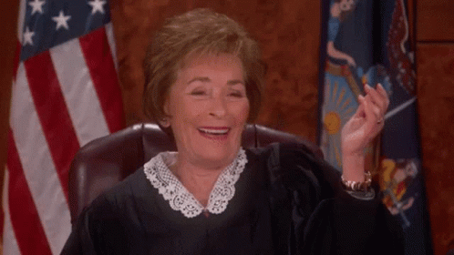 A Female Judge Is Smiling While Sitting In A Courtroom In Front Of An American Flag . GIF