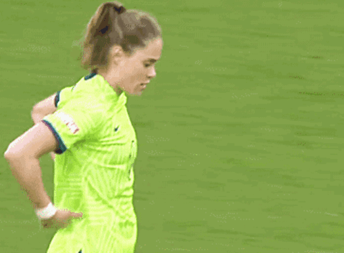 A Female Soccer Player In A Neon Green Jersey Is Standing On The Field . GIF