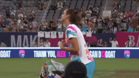 A Female Soccer Player Stands On The Field In Front Of A Banner That Says " Thank You Men " GIF
