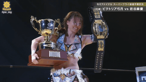 A Female Wrestler Holding A Trophy And A Belt That Says Victoria GIF
