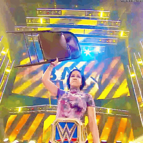 A Female Wrestler Holds A Chair Over Her Head While Wearing A W Belt GIF