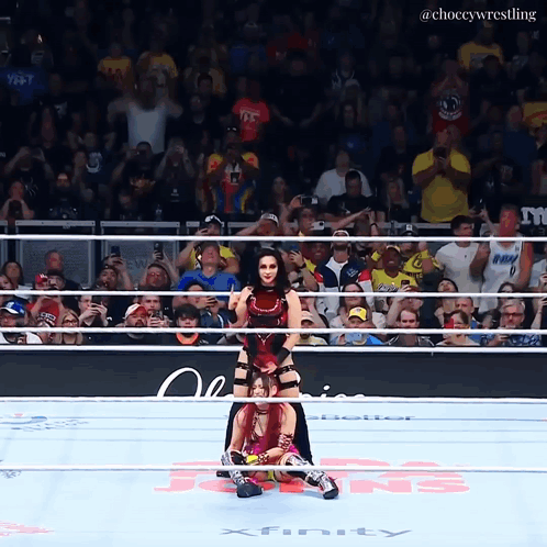 A Female Wrestler Is Being Lifted By Another Wrestler In A Ring That Says Xfinity On The Floor GIF