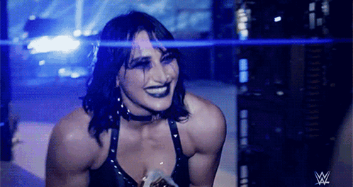 A Female Wrestler Is Smiling In Front Of A W Logo GIF