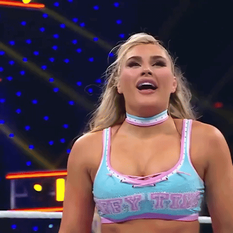 A Female Wrestler Is Standing In A Ring Wearing A Blue And Pink Top And Choker . GIF