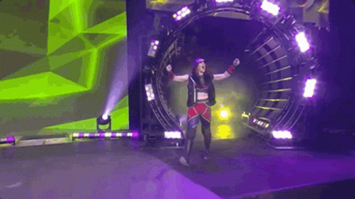 A Female Wrestler Is Walking Through A Tunnel On A Stage With Her Arms In The Air . GIF