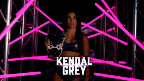 a female wrestler named kendal grey is standing in a dark room with pink lights behind her