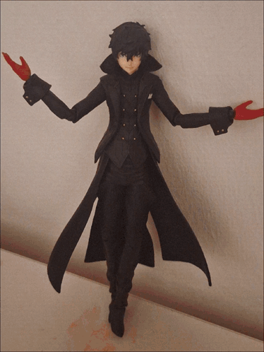A Figurine Of A Man In A Black Coat With Red Gloves Is Standing On A Table GIF