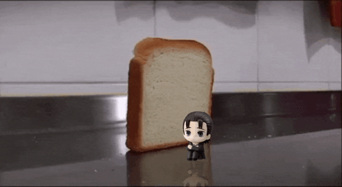 A Figurine Of A Man Is Standing Next To A Slice Of Bread . GIF